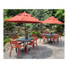 A red Grosfillex Cannes armchair next to a table on a patio with a red umbrella.