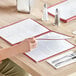 A woman sitting at a table with a burgundy Choice menu cover on it.