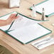 A person holding a green 8 1/2" x 11" menu cover with four pockets.