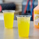 Two plastic cups of yellow Sqwincher Tropical Cooler on a table.