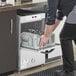 A man putting glasses in a Noble Warewashing underbar glass washer on a professional kitchen counter.