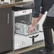 A high-temperature underbar glass washer with a pull-out rack being loaded with glasses.