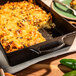 A Lodge cast iron roasting pan with a casserole dish of peppers and cheese in it.