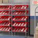 A Regency stationary slanted chrome shelf unit with red bins on it.