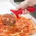 A person using an American Metalcraft stainless steel pizza cutter with a red handle to cut a pizza.