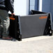 A man standing next to a black rectangular flood gate stanchion with orange text.