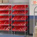 A Regency metal slanted shelf unit with red bins on it.
