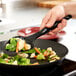 A person using a Vollrath slotted spoon to cook vegetables in a pan.