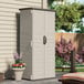 A Suncast vanilla vertical storage shed with a door on the side on a patio.