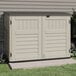 A vanilla Suncast horizontal storage shed with black doors sitting on the grass.