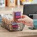 A person holding a bag of Sweet Sam's Individually Wrapped Streusel Coffee Cake in a basket on a counter.