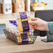 A hand holding a bag of Sweet Sam's lemon pound cakes in front of a bakery display counter.