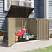 A Suncast sand storage shed with a wheelbarrow and gardening tools inside.