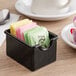 A black plastic sugar caddy with sugar packets inside.