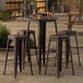 A Lancaster Table & Seating Alloy Series round copper bar height table with four backless barstools on a patio.