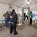 A security guard uses a Garrett PD6500i metal detector to screen a person in a blue jacket in a stadium concession stand line.