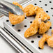 A Vollrath stainless steel false bottom in use picking up fried chicken.