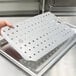 A hand holding a Vollrath stainless steel false bottom with holes in it.