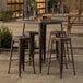 A Lancaster Table & Seating outdoor bar height table with four backless barstools on a patio.