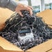 A hand holding a package in a box filled with Spring-Fill silver and black metallic paper shred.