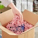 A hand holding a cardboard box with Spring-Fill Light Pink Crinkle Cut paper shred.