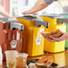 A person using a Heinz countertop pump to dispense mustard onto a plate of fried chicken.