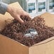 A hand reaching into a cardboard box filled with brown Spring-Fill Chocolate Crinkle Cut paper shred.