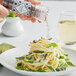 A hand grinding Maldon black peppercorns onto a plate of spaghetti with asparagus and basil.