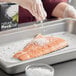A person sprinkling Tidman's Natural Rock Salt on a piece of fish.