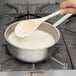 a person holding a wooden spoon over a pot of white liquid