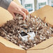 A hand holding a package in a cardboard box with Spring-Fill Kraft Monster Crinkle paper.