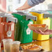 A person using a Heinz countertop sweet relish pump to dispense relish onto a hot dog.