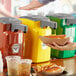 A person using a Heinz countertop mustard pump to pour mustard onto a hot dog.