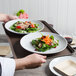 A person holding a Cambro non-skid serving tray with two plates of salad on a table.