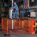 A man on a platform in a warehouse uses an Ideal Warehouse orange safety barrier.