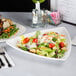 A table with a salad and a plate of meat on Tuxton white china plates.