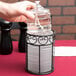 A hand holding a Sterno Liquid Candle Fuel cartridge over a table with a glass of water.