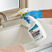 A hand in a blue glove holding a CLR Pro restroom cleaner spray bottle.