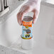 A gloved hand using CLR PRO Pressurized Drain Opener in a professional kitchen sink.