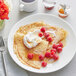 A plate of crepes with raspberries and Runamok Bourbon Barrel-Aged Maple Syrup served in a white cup.