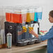 A woman pouring liquid into the Carnival King Triple Bowl Refrigerated Beverage Dispenser.