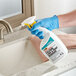 A person wearing blue gloves holding a bottle of CLR Calcium, Lime, and Rust Remover.