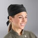 A woman wearing a black Uncommon Chef skull cap with ties smiling in a professional kitchen.