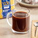 A glass mug of Lavazza coffee with a spoon next to it on a table.