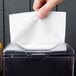 A hand putting a OneUp by Choice white dispenser napkin in a plastic dispenser.