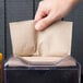 A hand putting a brown dispenser napkin in a dispenser.