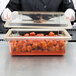 A person wearing a black coat holding a Cambro food storage box on a kitchen counter.