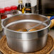 A Vollrath stainless steel vegetable inset pot with a spoon in it.