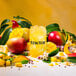 A glass of yellow Tractor Beverage Co. mango liquid with fruit and leaves on the rim.