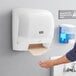 A woman using a Lavex white automatic paper towel dispenser.